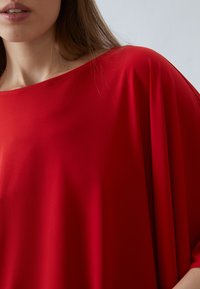 Rotes, leichtes, drapiertes Top mit weitem Ausschnitt und lockerer Passform. Glatte Textur mit minimaler Nahtführung, die ein lässiges Design hervorhebt.