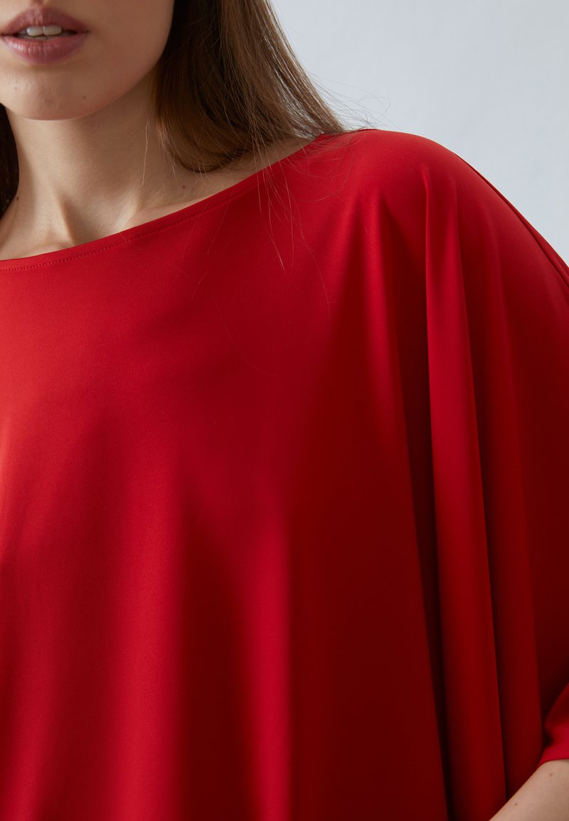 Top rosso leggero, drappeggiato, con una scollatura ampia e una vestibilità comoda. Texture liscia con cuciture minime, che mette in risalto un design casual.