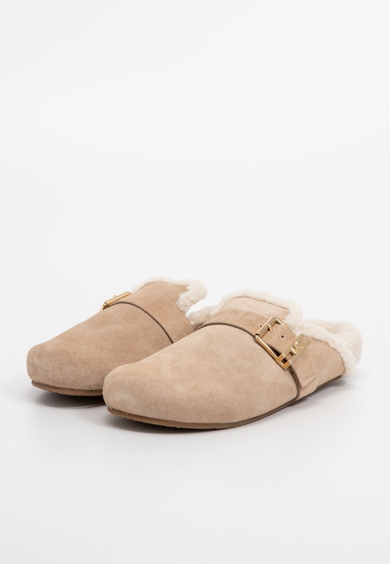 Pantoufles en daim beige avec une douce doublure en fourrure, design à bout fermé et accent en boucle dorée sur le côté. Semelle plate pour le confort.