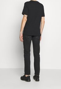 Schwarzes T-Shirt mit kurzen Ärmeln, lockere Passform. Getragen mit dunklen Jeans und schwarzen Sneakern. Einfaches Design, keine sichtbaren Muster oder Logos.