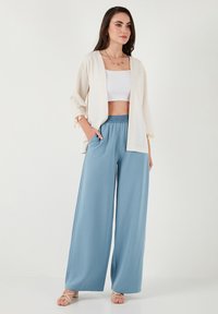 Cardigan leggero in crema con maniche ¾, abbinato a pantaloni leggeri blu chiaro con vita elasticizzata e texture morbida.