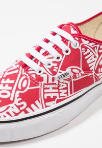 Rote Leinenschuhe mit weißen grafischen Mustern, ausgestattet mit einem weißen Schnürdesign, flacher Sohle und Vans-Logo an der Seite.
