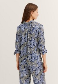 Floral-patterned blouse in navy and cream with rolled sleeves, round neckline, and a back pleat for ease of movement.