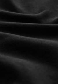 Tissu noir avec une surface lisse et légèrement texturée, présentant des plis doux et un motif uniforme, mettant en avant sa souplesse.