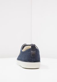 Denim sneakers i marinblått med en vit gummi sula. Har en bakre dragrem i mörkt material och subtil branding på sidan.