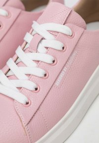 Sneaker in finta pelle rosa chiaro con lacci e occhielli bianchi. Presenta una superficie testurizzata e la scritta 'DESIGNED BY W' impressa di lato.