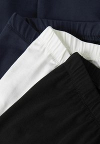 Trois ceintures élastiques de pantalons pliées en bleu marine, blanc et noir, empilées près les unes des autres sur un fond sombre.