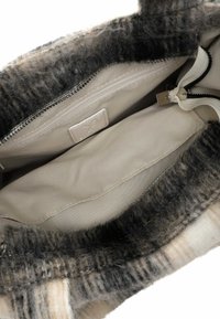 Interior de bolso con pelaje y patrón de cuadros, forro de tela beige, bolsillo interior con cremallera y cordón blanco con extremo metálico.