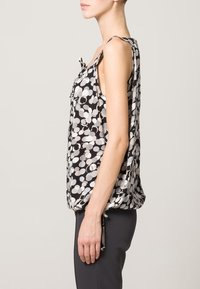 Czarny i biały bezrękawnik z wzorem o różnych rozmiarach okręgów, z bocznymi wiązaniami i luźnym krojem, wykonany z lekkiego materiału.