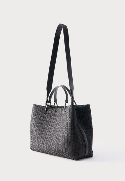 Μαύρη υφαντή δερμάτινη τσάντα ώμου με δύο κοντά χερούλια και ένα μακρύ ρυθμιζόμενο λουρί ώμου, που στέκεται πάνω σε απλό φωτεινό φόντο.