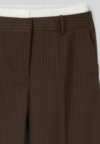 Pantalon rayé brun avec une ceinture élastique blanche, présentant un devant plat, des poches angulaires et des plis ajustés pour la forme et le design.