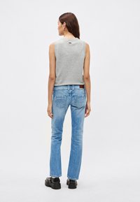 Sivý top bez rukávov, svetlomodré džíny s rovnými nohavicami a čierne platformové topánky. Výrazný detail s rozopínaním na chrbte na tope.