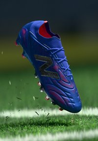 Modrá fotbalová kopačka s texturovaným svrškem, černými akcenty a růžovými detaily na podrážce. Navrženo pro výkon na travnatých površích.
