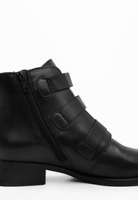 Czarne skórzane botki do kostki z zaokrąglonym noskiem, bocznym zamkiem błyskawicznym oraz trzema regulowanymi paskami. Gładka tekstura i minimalistyczny design.