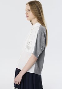 Camisa de manga corta con un frente blanco y una parte trasera de punto gris, con un bolsillo con parche y acentos de botón en las mangas. Tejido texturizado.