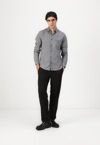 Button-up shirt in black and white check pattern, long sleeves, with a patch pocket. Paired with black trousers and shiny black shoes.