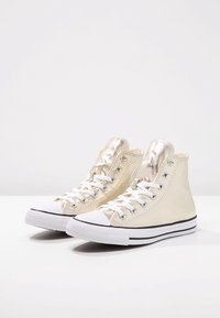 Sneakers alte in pelle color crema con dettagli in oro metallizzato, puntale in gomma bianca e suola a strisce nere. Fori per lacci e lacci inclusi con dettagli accurati.