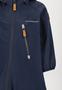 Marinblå jacka med dragkedja och silverfärgad draghandtag, beige detaljer och hög krage. Tillverkad av mjukt, hållbart material med slim fit.