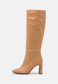 Bottes en cuir beige jusqu'aux genoux avec un bout pointu et un talon épais robuste. Texture lisse avec des coutures minimales et une silhouette élégante.