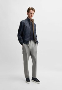 Marinflighistjacka med brun insida, grå skräddarsydda byxor med sidofickor och svarta sneakers. Slät tyg och strukturerad passform.