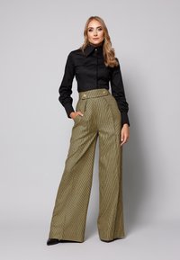 Czarna koszula z guzikami, z wysokim kołnierzem i usztywnionymi rękawami, zestawiona z wysoką w talii, wzorzystą w kratkę, szeroką spódnicą z przednimi kieszeniami.