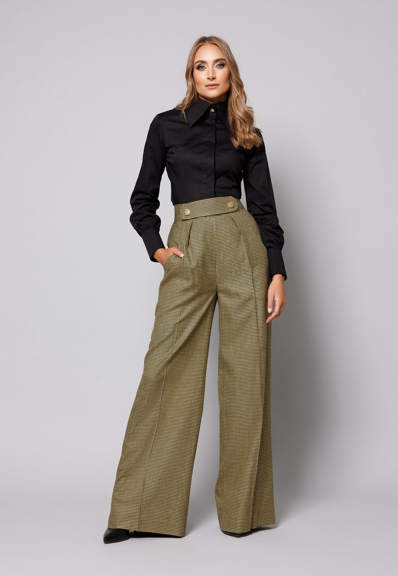 Czarna koszula z guzikami, z wysokim kołnierzem i usztywnionymi rękawami, zestawiona z wysoką w talii, wzorzystą w kratkę, szeroką spódnicą z przednimi kieszeniami.