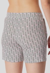 Korte broek gemaakt van lichtgewicht stof, met zwart-witte geometrische patronen en roze accenten, elastische tailleband en een relaxte pasvorm.