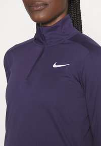 Närbild av en person som bär en mörklila Nike långärmad zip-up-tröja med Nike swoosh-logotypen på bröstet.