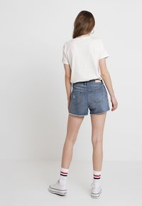 Shorts di denim con orlo sfrangiato, vita alta, colore azzurro chiaro e due tasche posteriori. Abbinati a una t-shirt bianca e sneakers bianche.