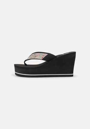 Sort kileflip-flop sandal med tyk sål, sorte stofstropper dekoreret med flerfarvede rhinsten på en ensfarvet baggrund.