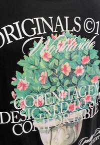 Blomstrende busk med rosa blomster i dekorativ potte, overlagt med hvit stilisert tekst som inkluderer "ORIGINALS," "Worldwide," "Copenhagen," og "Comfortable."