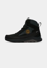 Scarpe da trekking nere con accenti grigi, materiale Gore-Tex impermeabile, superficie texture, suola resistente e logo prominente sul lato.