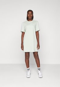 Robe de sport vert clair à manches courtes, dotée d'un col rond et d'accents discrets de trois rayures sur les épaules. Associée à des baskets blanches.