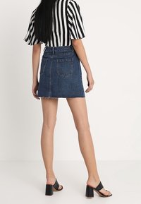 Falda mini de mezclilla con dobladillo deshilachado, cinco bolsillos; combinada con una blusa de rayas en blanco y negro y sandalias de tacón cuadrado negras.