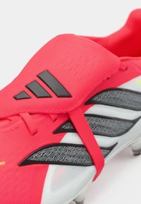 Κόκκινα αθλητικά παπούτσια με λείο συνθετικό επάνω μέρος, που διαθέτουν μαύρο λογότυπο με τρεις ρίγες και γκρι υφασμάτινες λεπτομέρειες στα πλαϊνά.