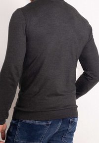 Dunkelgraues Sweatshirt mit langen Ärmeln und rundem Halsausschnitt. Weicher, strukturierter Stoff und eng anliegender Bund. Kombiniert mit blauen Jeans.