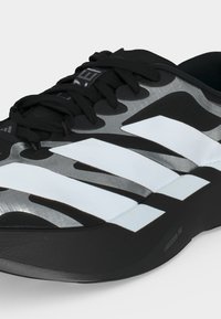 Chaussure de sport noire et grise avec des bandes diagonales blanches, des lacets noirs et le texte "LIGHTSTRIKE PRO" sur le bord de la semelle.