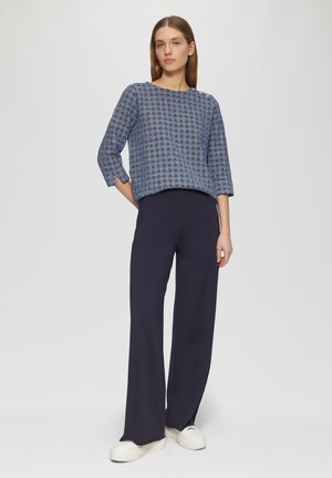 Blue patterned top with three-quarter sleeves, paired with navy wide-leg trousers and white sneakers. The fabric is textured and soft.