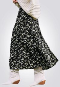 Jupe longue noire à fleurs avec des motifs de fleurs blanches et vertes, design à volants, associée à des bottes à talons blanches. Texture de tissu douce.
