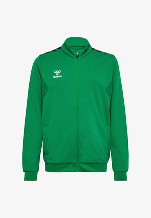 Deux enfants debout côte à côte, portant des vestes de sport vertes, des pantalons noirs et des baskets noires sur un fond blanc uni.