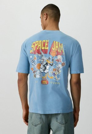 Man wearing blue t-shirt featuring Space Jam characters Bugs Bunny, Daffy Duck, and others playing basketball with "Space Jam 1996" text.