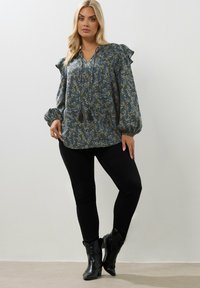 Blus med blommönster i blått och gult, med volangärmar, V-ringning och tofsar. Matchad med svarta tajta byxor och stövlar.