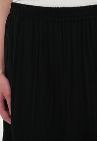 Gonna nera con un tessuto strutturato e stropicciato. Presenta una vita elasticizzata e un orlo a strati, che enfatizzano un design fluido.