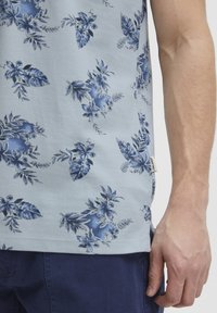 Ljusblå kortärmad skjorta med ett blommigt mönster i mörkblå nyanser. Tyget ser mjukt ut med en lätt textur. En etikett syns vid fållen.