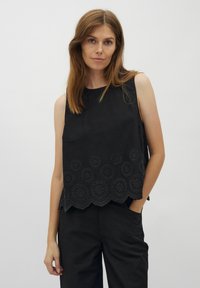 Zwarte mouwloze top met een scalloped zoom en cirkelvormige borduursels. Gemaakt van een textiel met een eenvoudige, strakke ontwerp.