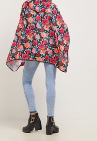 Kwiatowy płaszcz na czarnym tle z różowymi i pomarańczowymi różami. Posiada kaptur, wykonany jest z lekkiego materiału i ma zwiewny fason.