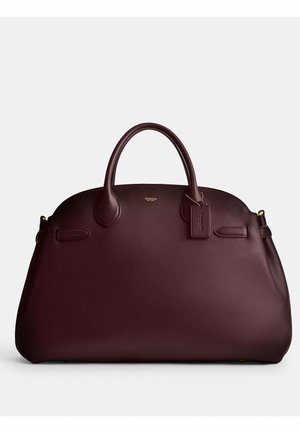 Sac à main Coach en cuir marron foncé avec doubles poignées et étiquette en cuir attachée, présenté sur un fond clair uni.
