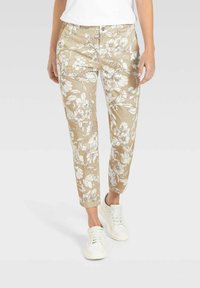 Blumengemusterte, beige Hose mit schlankem Schnitt und knöchellang, kombiniert mit weißen Sneakers, aus weichem, glattem Stoff.