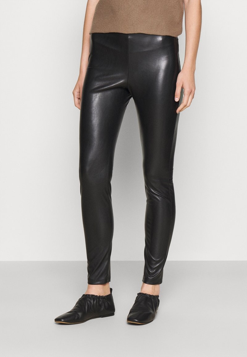 Svarta läderleggings med smal passform, slät textur, hög midja och minimala sömmar, i kombination med svarta, mjuka platta skor.