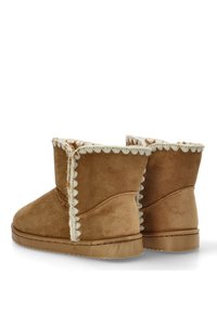 Botas de tobillo de ante beige con una superficie texturizada, que presentan un borde ondulado blanco en el borde superior y una suela plana de goma.